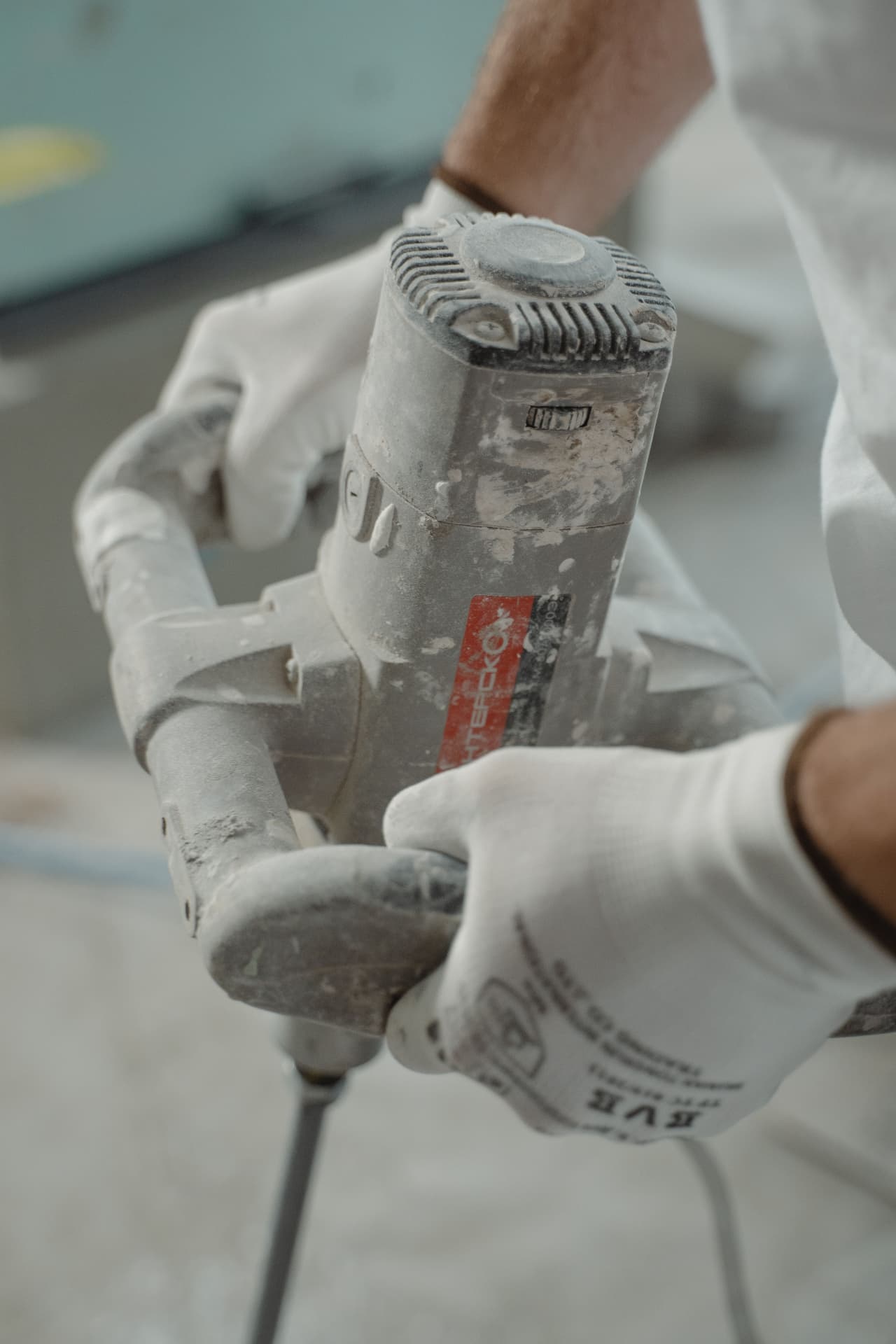 Handwerker mit Handschuhen bedient eine staubbedeckte Bohrmaschine auf der Baustelle